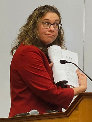 Woman standing at podium showing book page to audience